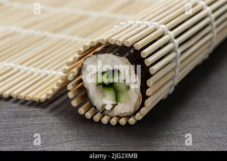 Il sushi di Nori rotola su un tappeto di bambù. Primo piano. Sfondo grigio Foto Stock