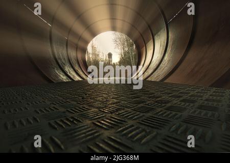 Vista attraverso un tubo metallico. Sullo sfondo tra gli alberi si trova una torre d'acqua. Arte con angolazione rara Foto Stock