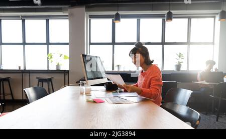 Donna d'affari asiatica sorridente che guarda la fotografia al computer desk in ufficio Foto Stock