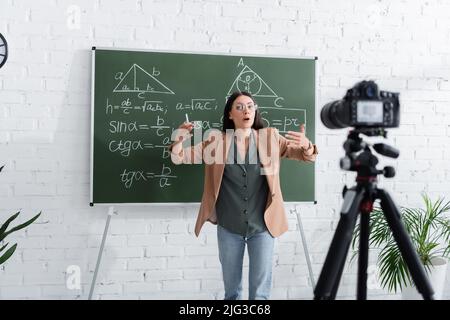 Insegnante che parla vicino a formule matematiche su lavagna e fotocamera digitale in classe Foto Stock