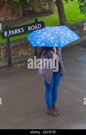 Visitatore con ombrello in piedi nella pioggia battente a Parks Road, Oxford, Oxfordshire Regno Unito in una giornata piovosa bagnata nel mese di agosto Foto Stock