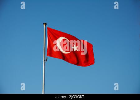 La bandiera della Turchia soffia nel vento contro un cielo blu. Foto Stock