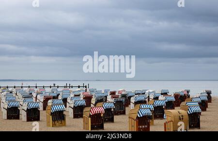 07 luglio 2022, Schleswig-Holstein, Travemünde: Solo poche persone sono fuori e circa sotto il cielo coperto tra le sedie da spiaggia per lo più chiuse sul Mar Baltico vicino a Travemünde. Dopo Schleswig-Holstein e Meclemburgo-Pomerania occidentale, le vacanze estive sono iniziate ad Amburgo giovedì. Foto: Christian Charisius/dpa Foto Stock