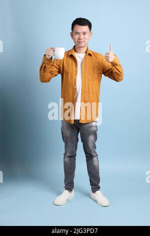 L'uomo asiatico LGBTQ con camicia gialla in piedi su sfondo blu. Foto Stock