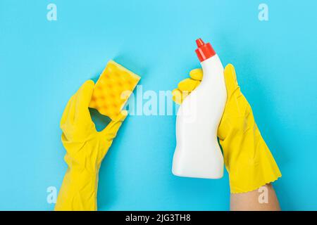 Le mani di una casalinga in guanti protettivi di gomma gialli tengono una bottiglia di prodotti chimici domestici e uno straccio. Detergente per varie superfici nel kitc Foto Stock