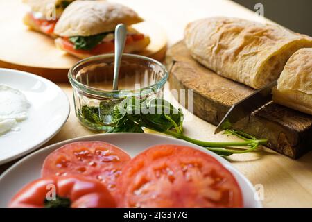 Preparazione dei sandwich italiani PANINI con pomodori e basilico al tavolo Foto Stock