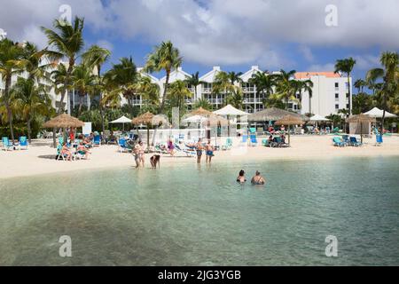 ORANJESTAD, ARUBA - 4 DICEMBRE 2021: Piscina del Renaissance Ocean Suites Hotel e spiaggia sabbiosa con palme e sedie da spiaggia Foto Stock