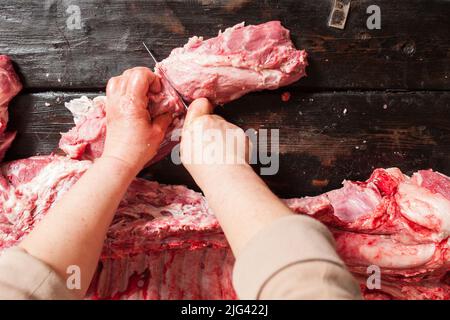 Macellaio taglia il trotto di maiale crudo. Sfondo di legno Foto Stock