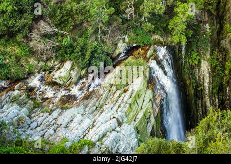 Guardando giù sul bordo di una scogliera, con una cascata che precipita giù esso, nella strada di giardino, Sudafrica. Foto Stock