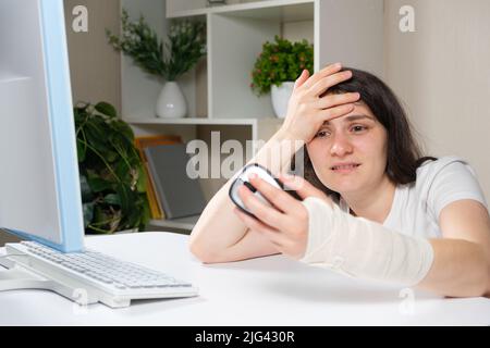 Una donna con un bendaggio elastico sul polso si siede di fronte ad un computer, sindrome del tunnel carpale Foto Stock
