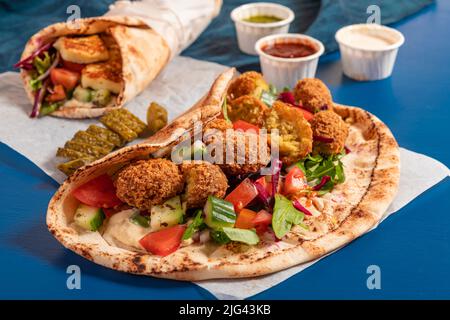 Tradizionali halloumi arabi alla griglia mediterranei e falafel, hummus e verdure in involtini di pane piatto con erbe e una varietà di salse Foto Stock