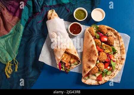 Tradizionali halloumi arabi alla griglia mediterranei e falafel, hummus e verdure in involtini di pane piatto con erbe e una varietà di salse Foto Stock