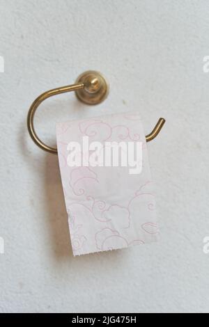 Carta igienica rosa appesa su un supporto di carta igienica dorata su una parete leggera del bagno Foto Stock