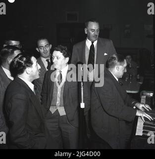 1950s, quadro storico che mostra diversi acciaierie gallesi riuniti intorno a un pianoforte, avendo una canzone nel sociale società dopo il lavoro, Abbey Steel Works, Port Talbot, Galles, Regno Unito. Foto Stock