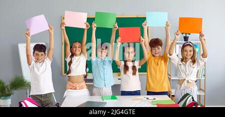 I ragazzi e le ragazze della scuola elementare felici hanno in mano fogli di carta colorati in classe. Foto Stock