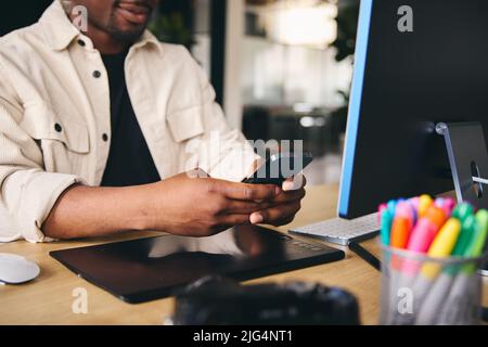 Primo piano Anonimo giovane uomo nero creativo in ufficio moderno seduta alla scrivania utilizzando il telefono cellulare Foto Stock