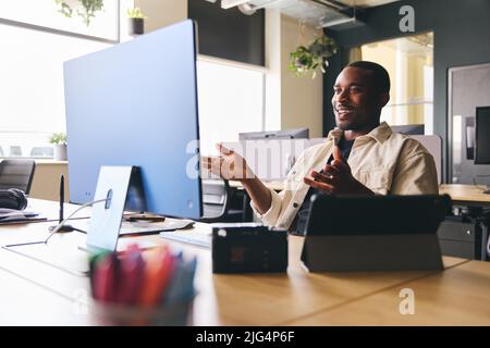 Giovane uomo nero che ha videoconferenza chiamata in remoto con il team in ufficio moderno seduto alla scrivania sul computer Foto Stock