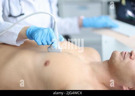 Medico che tiene la macchina ad ultrasuoni sul petto dell'uomo in clinica Foto Stock