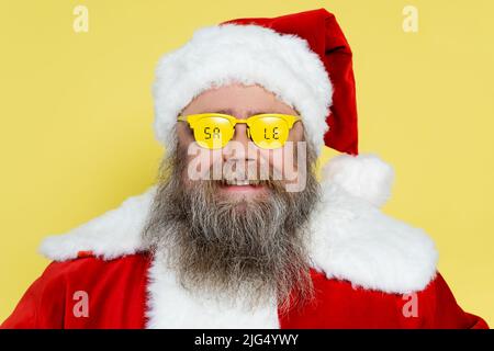 uomo sorridente e chubby in costume di natale e occhiali con vendita scritta isolato sul giallo Foto Stock