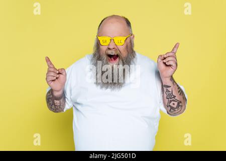 uomo sovrappeso audace e bearded in occhiali con lettere di vendita puntando con le dita isolate sul giallo Foto Stock