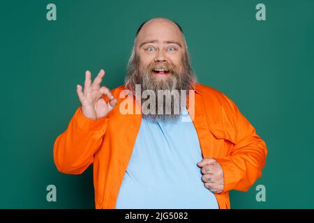 uomo emozionato e di taglia più in camicia arancione con cartello "ok" isolato sul verde Foto Stock