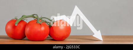 Il prezzo dei pomodori e delle verdure. Raccolto vegetale difettoso. Pomodori freschi rossi maturi con rametti sul tavolo. Il grafico è rivolto verso il basso. Foto Stock