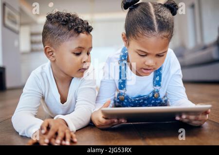 Due bambini giovani di razza mista che usano un tablet digitale mentre si trovano insieme sul pavimento a casa. Giovani fratelli e sorelle che navigano su Internet Foto Stock