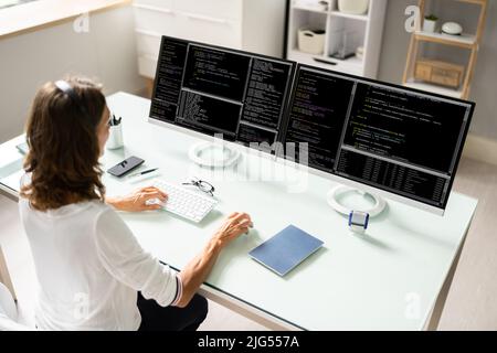 Programmatore femminile che lavora su più schermi di computer Foto Stock