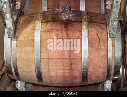 primo piano di una botte di vino di quercia in una moderna rastrelliera metallica in una cantina commerciale che mostra le macchie di vino e la consistenza del legno Foto Stock