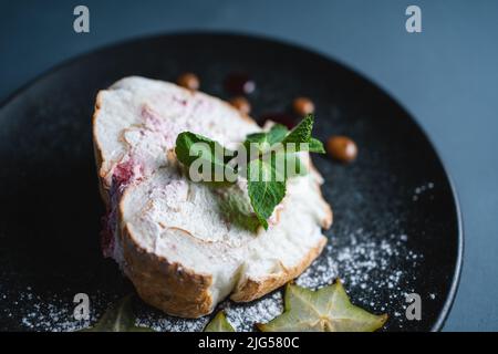 torta di meringa con crema di mascarpone, menta e carambola su sfondo nero Foto Stock