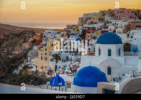 Vista panoramica panoramica del villaggio di Oia al tramonto con l'iconica chiesa a cupola blu in primo piano, Santorini, Grecia Foto Stock