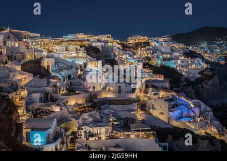 Vista panoramica di notte del villaggio di Oia a Santorini, con le sue case tipiche che ospitano suite e boutique hotel illuminati Foto Stock