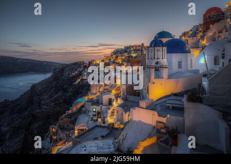 Vista panoramica panoramica del villaggio di Oia al tramonto con l'iconica chiesa a cupola blu in primo piano, Santorini, Grecia Foto Stock