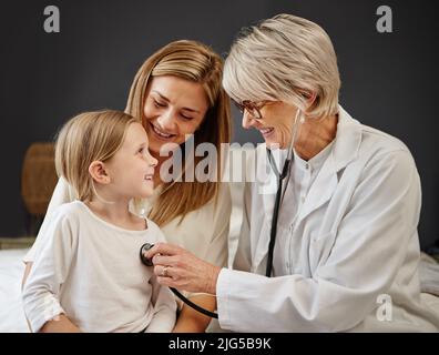 Shell ottenere l'aiuto di cui ha bisogno. Shot di un medico che esamina una bambina e sua madre con uno stetoscopio a letto a casa. Foto Stock