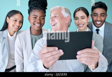Thats un'immagine impressionante. Studio girato di un gruppo diversificato di uomini d'affari aziendali utilizzando un tablet per prendere selfie su sfondo blu. Foto Stock