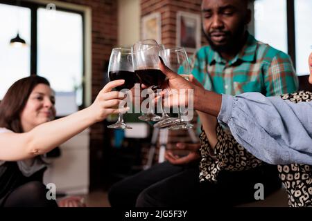 Felice sorridente persone diverse calici occhiali durante la celebrazione del compleanno evento. Gioioso gruppo multirazziale di migliori amici che tostano i vini mentre vi godete la festa del vino a casa. Foto Stock