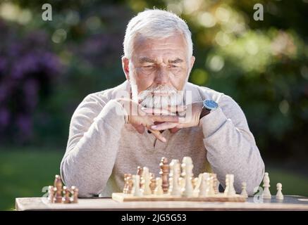 Un po' di fortuna, un po' di logica. Colpo di un uomo anziano che gioca una partita di scacchi fuori. Foto Stock