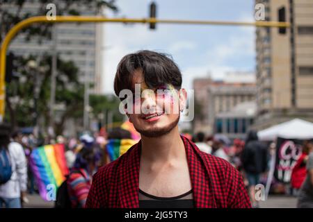 L'uomo con bandiera lgtbiq+ dipinta sul viso sorride mentre frequenta la celebrazione dell'orgoglio a Bogotà. Foto Stock