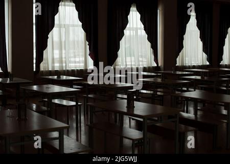 Tende nella sala da pranzo. Un sacco di tavoli. Luce dalle grandi finestre. Banchi in fila. Foto Stock