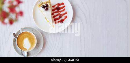 Torta al biscotto di ciliegia, lampone e tazza di cappuccino su tavola di legno all'aperto. Decorazioni di fiori rosa nella terrazza della caffetteria. Striscione extra largo. Spazio di copia. Foto Stock