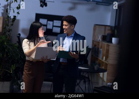 Professionisti asiatici maschi e femmine con notebook e report discutere di dati in ufficio di notte Foto Stock