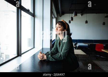 Giovane donna d'affari asiatica pensierosa che guarda attraverso la finestra in ufficio creativo Foto Stock
