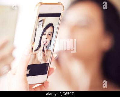 Questo specchio funziona per me. Scatto di una ragazza bella usando il suo telefono come uno specchio mentre applica il rossetto a casa. Foto Stock