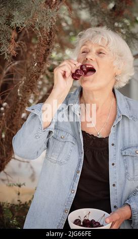 Donna anziana che tiene una ciotola di ciliegie mature Foto Stock