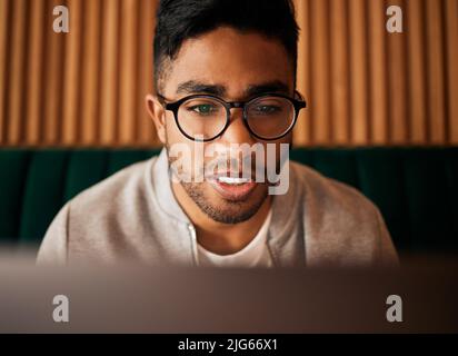 .. Primo piano di geeky giovane uomo indiano indossare occhiali mentre si legge qualcosa di interessante e seduto all'interno. Uomo che indossa gli occhiali mentre legge in linea Foto Stock