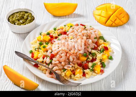 gamberetti cotti per insalata conditi con porridge di miglio con piselli verdi, mango, peperoni rossi su piatto bianco su tavola di legno bianco, con ingredienti Foto Stock