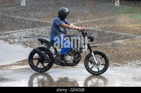 SAMUT PRAKAN, THAILANDIA, 28 2022 MARZO, Un uomo corre in una pioggia pesante su una moto Foto Stock