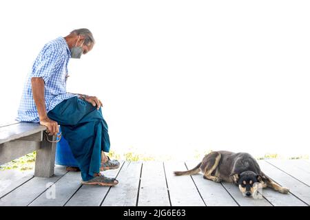 SAMUT PRAKAN, THAILANDIA, Apr 14 2022, un vecchio uomo si siede in controluce con un cane che giace sul pavimento Foto Stock