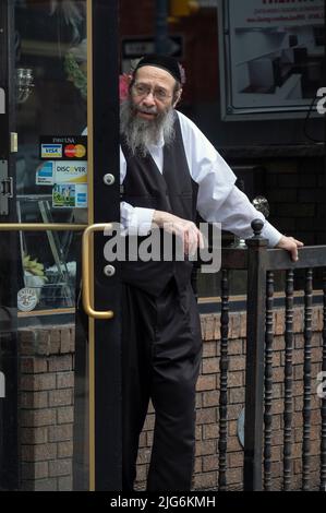 Un uomo ebreo hasidico più vecchio si trova fuori dal suo negozio ottenendo un soffio di aria fresca. Su Lee Avenue a Williamsbrg, Brooklyn, New York City. Foto Stock