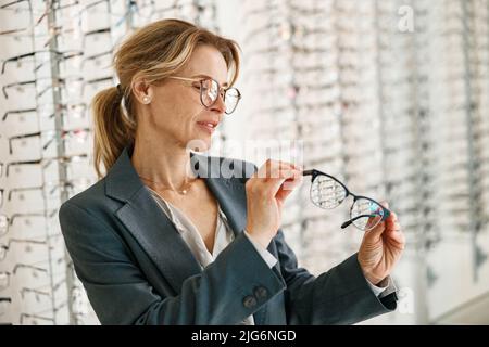 Donna in giacca sceglie tra due bicchieri in un negozio di ottico Foto Stock